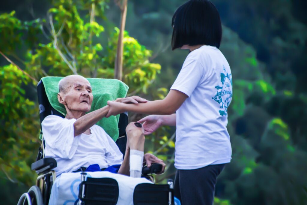 Image of a caregiver holding hands of an aged lady on a wheelchair.